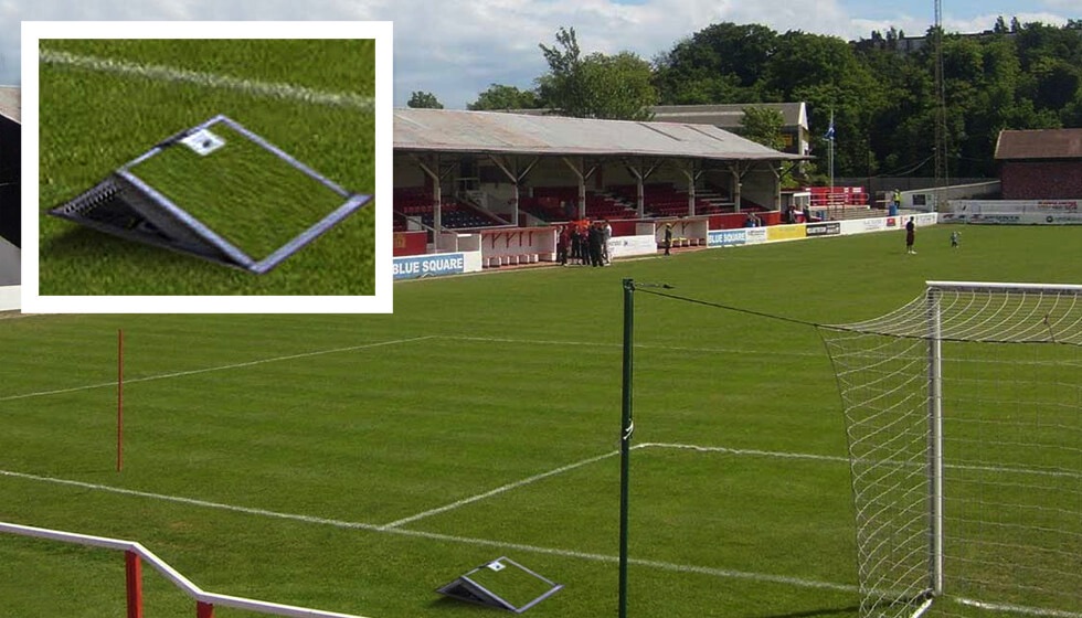 A flip-lid in-ground service unit installed on the edge of a football pitch, providing access to power and water to assist with maintaining the pitch.